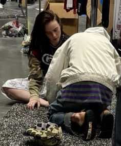 two people are sitting on the ground looking at something in front of them and one person is leaning over