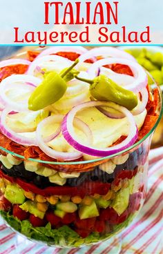 a layered salad in a glass bowl with red onions, tomatoes and green peppers on top