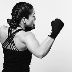 a woman wearing black boxing gloves and holding her fist in the air with both hands