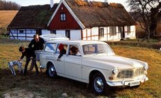 an old car parked in front of a house with two people standing next to it