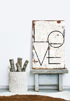 an old wooden sign sitting on top of a white table next to a basket filled with branches