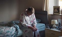 a woman sitting on top of a bed next to a night stand and telephones