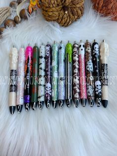 several pens are lined up on a white fur covered surface with pine cones in the background