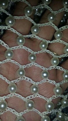 a person's hand is covered in pearls and lace, with their fingers on the net