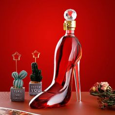 a red shoe shaped bottle sitting on top of a table next to cacti