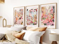 three posters on the wall above a bed with pillows and blankets, in front of a lamp