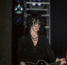 a woman playing a guitar in front of a microphone and stage lights on the other side of her face