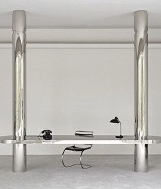 an office desk with two metal columns and a chair in front of it, against a white wall