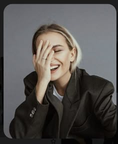 a woman with blonde hair smiling and holding her hands to her face while wearing a black jacket