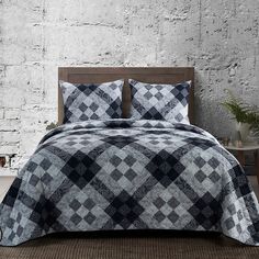 a bed with black and white checkered bedspread in front of a brick wall