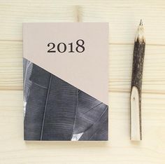 a book with a pen next to it on top of a wooden table near a pair of scissors