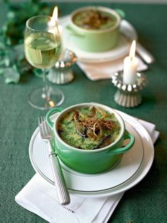 a green bowl filled with soup sitting on top of a white plate next to a glass of wine