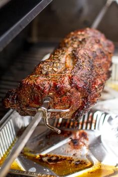 a large piece of meat is being cooked on a grill with tongs in it