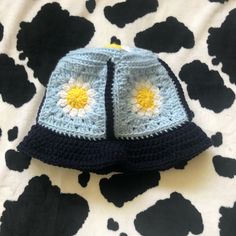 a crocheted hat on top of a cow print blanket with yellow and blue flowers