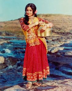 a woman is standing on rocks with a pot in her hand and wearing a sari