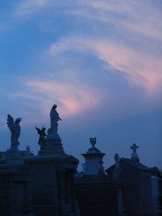 the silhouette of statues against a blue sky with clouds in the background