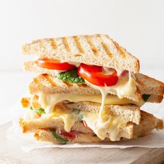 a grilled cheese and tomato sandwich on a wooden cutting board with a white background