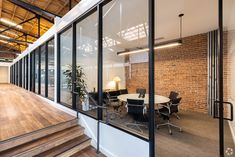 an open office with wooden floors and glass walls on one side, stairs leading up to the second