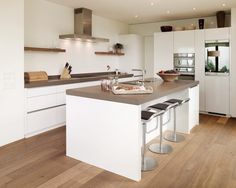 a modern kitchen with white cabinets and wood flooring, an island counter has two stools on it