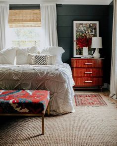 a bed sitting in a bedroom next to a window with white drapes on it