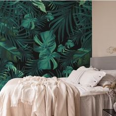 a bed with pillows and blankets in front of a green leafy wallpaper design