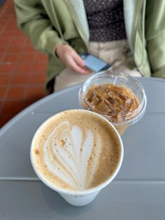 a person sitting at a table with a cup of coffee and a cell phone in their hand