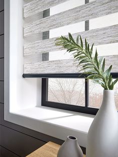 a white vase sitting on top of a wooden table next to a window sill