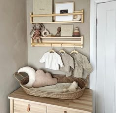 a baby's room with clothes hanging on the wall and wooden shelves above it