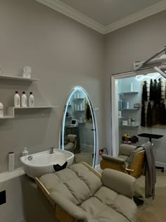 a hair salon with an oval mirror and white sink in the center, along with two tan leather recliners