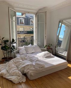 an unmade bed sitting on top of a hard wood floor next to two windows