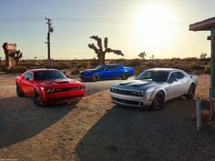 three different colored cars parked in front of a gas station with cactus trees and sun behind them