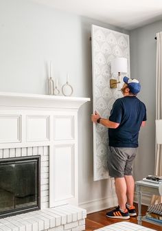 a man standing next to a fireplace in a living room with a white painted wall