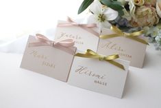 three place cards with bows on them are sitting next to a bouquet of white and pink flowers