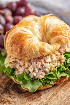 a croissant sandwich with meat and lettuce sits on a cutting board next to grapes