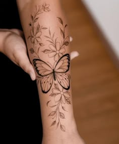 a woman's arm with a butterfly tattoo on it and flowers around the wrist