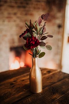 a vase filled with flowers sitting on top of a wooden table next to a fire place