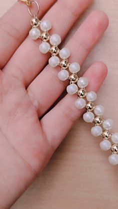 a hand is holding a gold and white beaded bracelet with pearls on it's sides