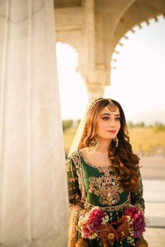 a woman in a green and gold outfit standing next to a white pillar with flowers on it