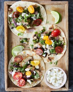 three tortillas with tomatoes, lettuce and other toppings on a wooden tray