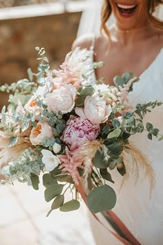 a woman in a wedding dress holding a bridal bouquet and laughing at the camera