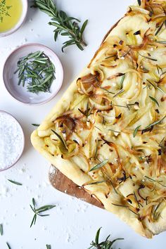 a pizza with onions and herbs on it next to some dipping sauces in small bowls