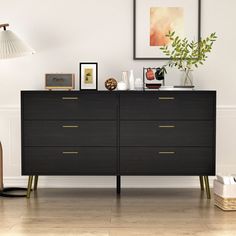 a room with a dresser, lamp and pictures on the wall above it that is decorated in black and gold