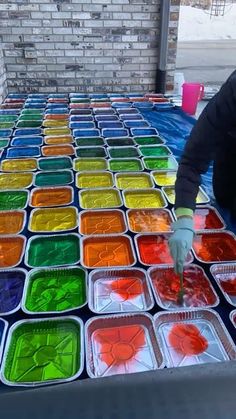 a man is painting on a table with many colors in plastic trays and gloves