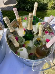 several bottles of champagne are in ice buckets on a table outside with other items