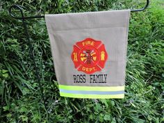 a fire department banner hanging from a metal pole in the grass with bushes behind it