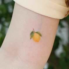 a small orange tattoo on the left inner arm, with green leaves and an orange on it's side