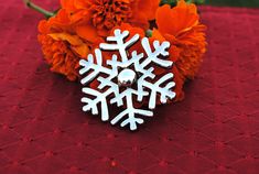 a snowflake brooch sitting on top of a table next to orange flowers