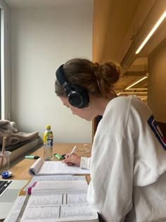 a woman sitting at a desk in front of a laptop computer wearing headphones and writing