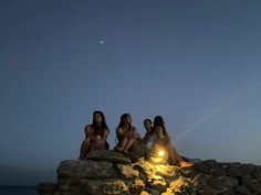 three women sitting on rocks at the edge of the ocean with their flashlight in their hand