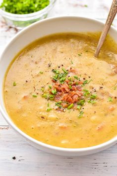 a white bowl filled with soup on top of a wooden table next to a spoon